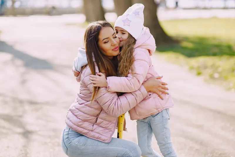 A mother and daughter embracing warmly in a sunny park
