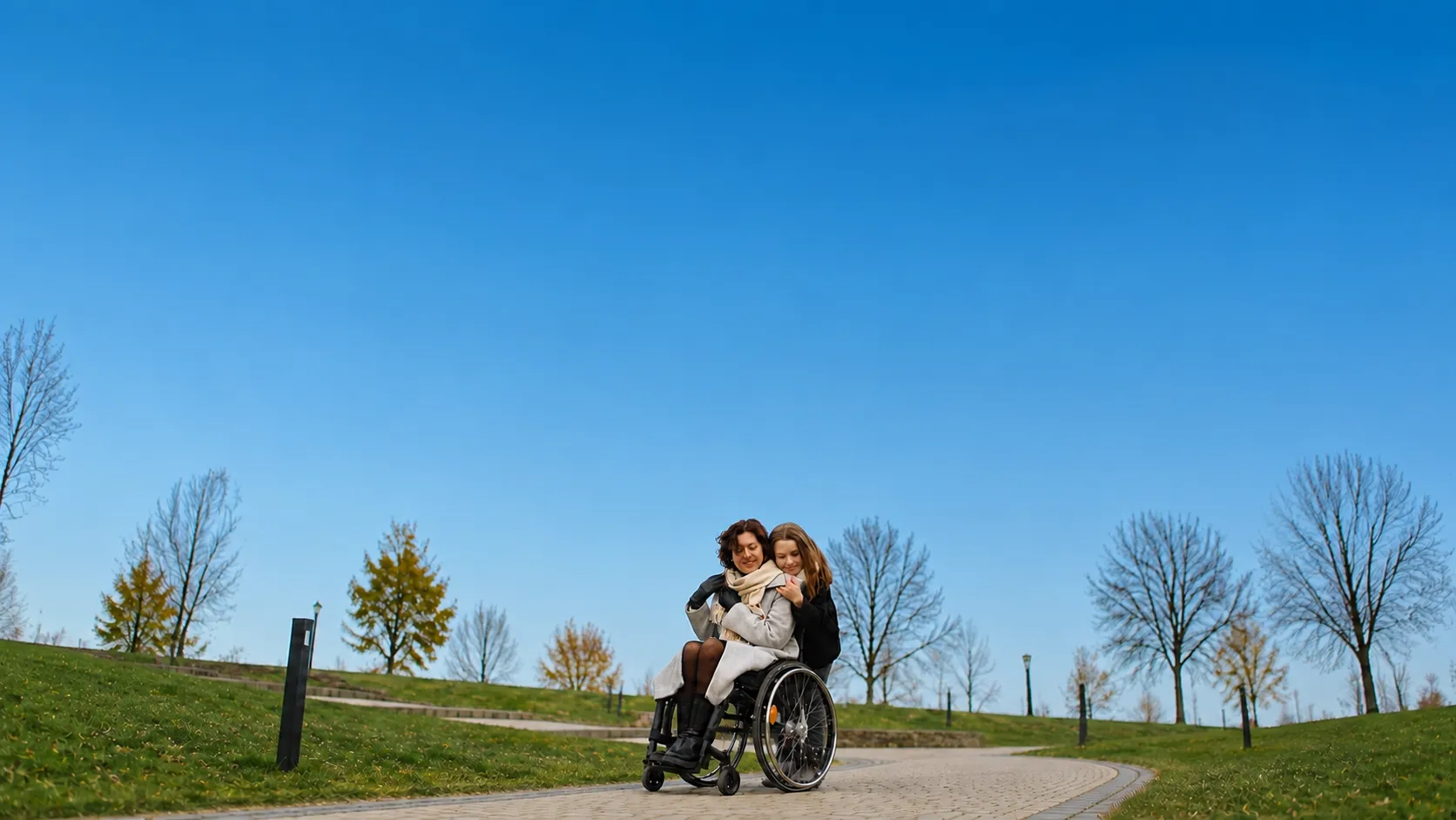 A woman using a wheelchair sharing a warm, happy moment with a young companion on a park path