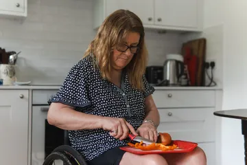 A woman using a wheelchair preparing vegetables in her own kitchen
