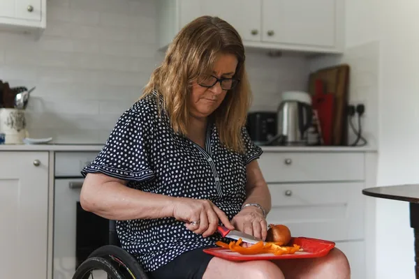 A woman using a wheelchair preparing vegetables in her own kitchen