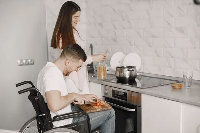 A man using a wheelchair preparing food in the kitchen alongside a support worker
