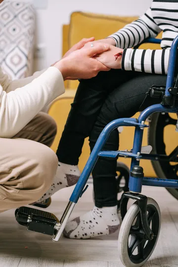 A support worker crouching to hold the hand of a person using a wheelchair