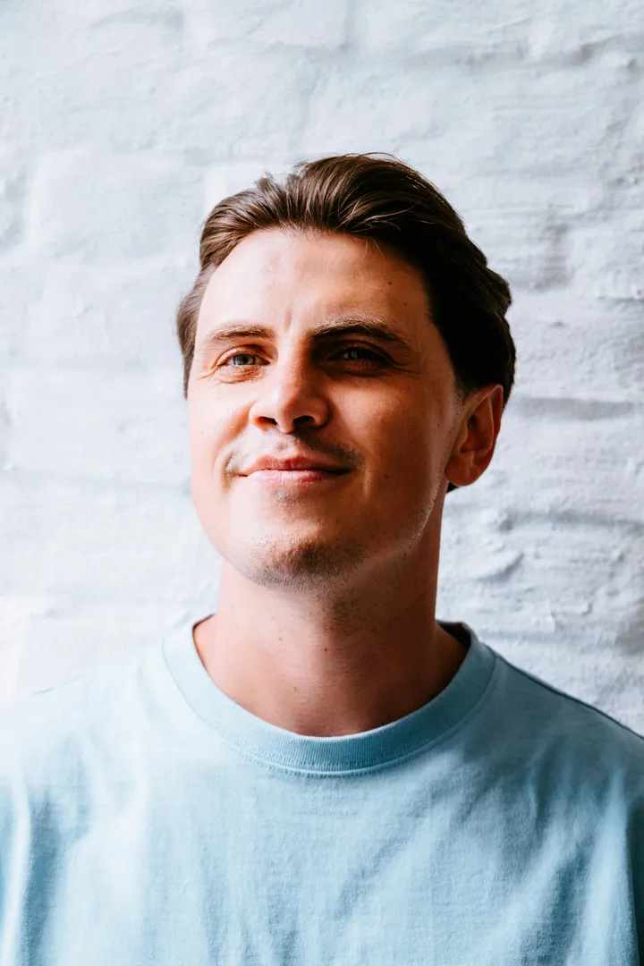 A man smiling warmly against a light wall